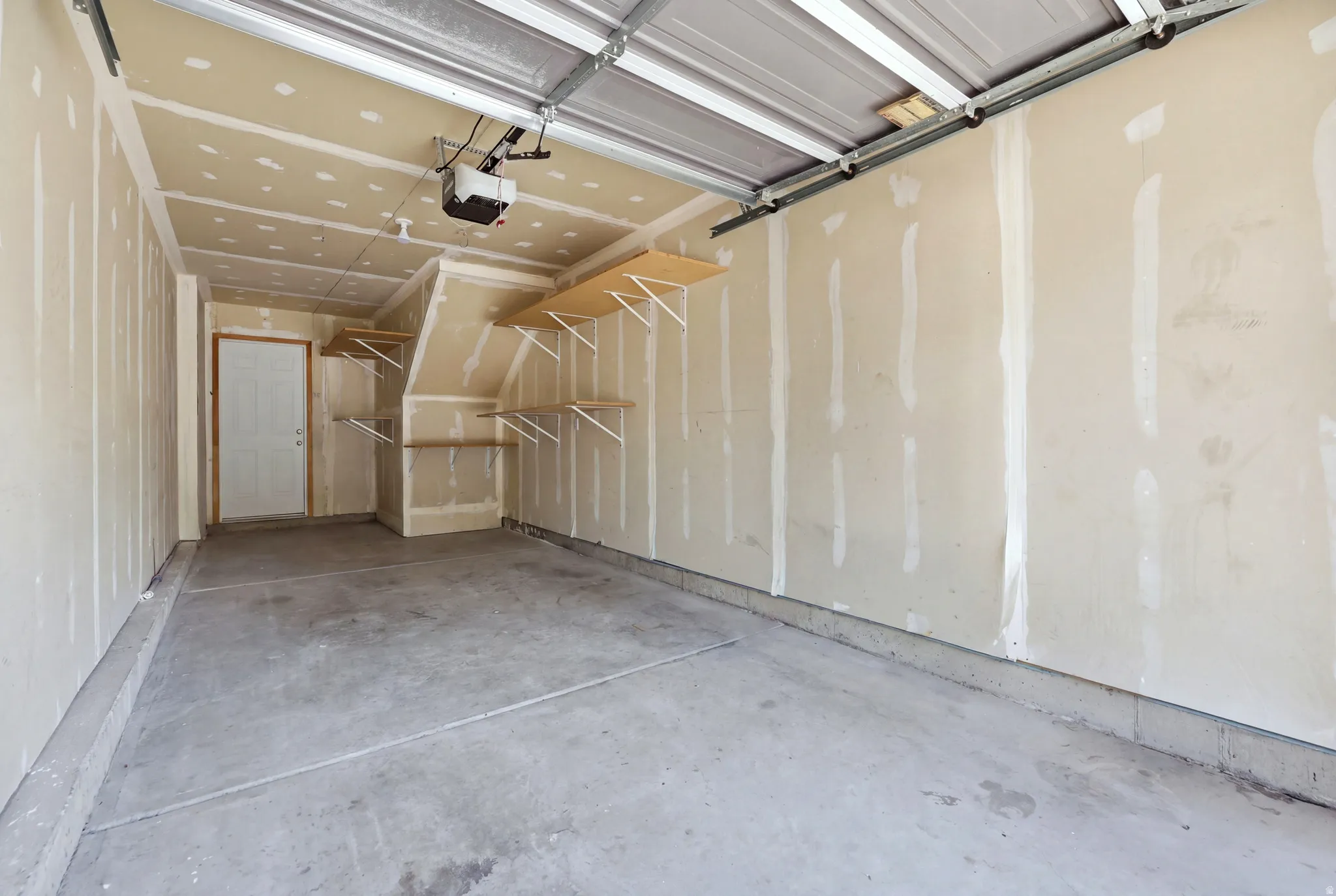 Concrete flooring, built-in wall shelving, garage door opener, and a side access door