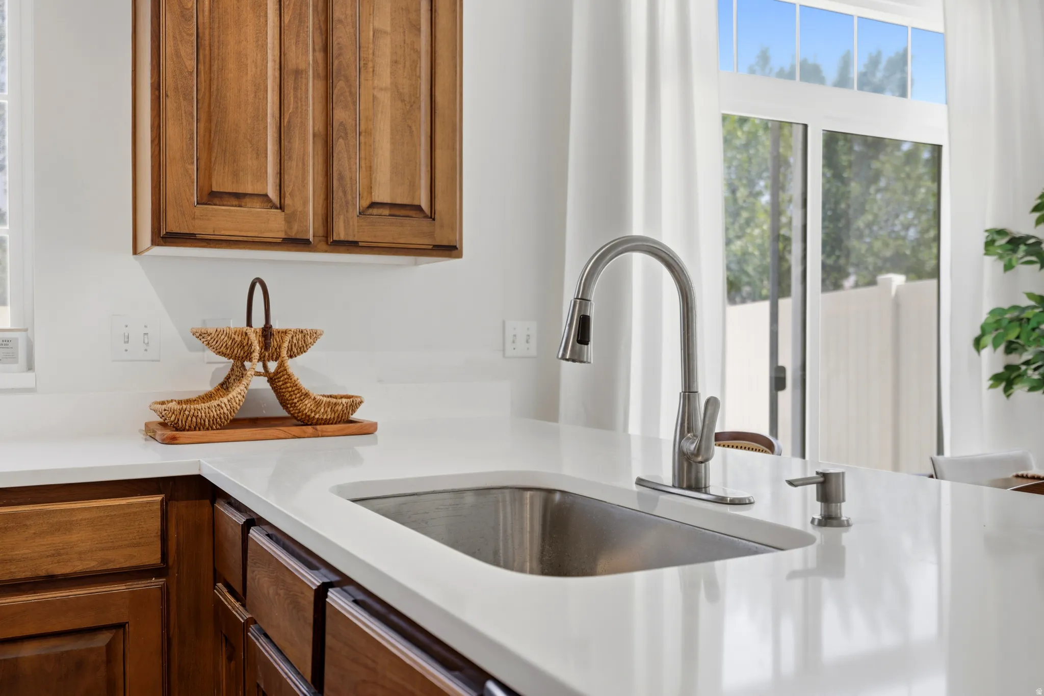 Stainless steel sink with a pull-down faucet, white solid surface countertop, and wood-finish cabinetry
