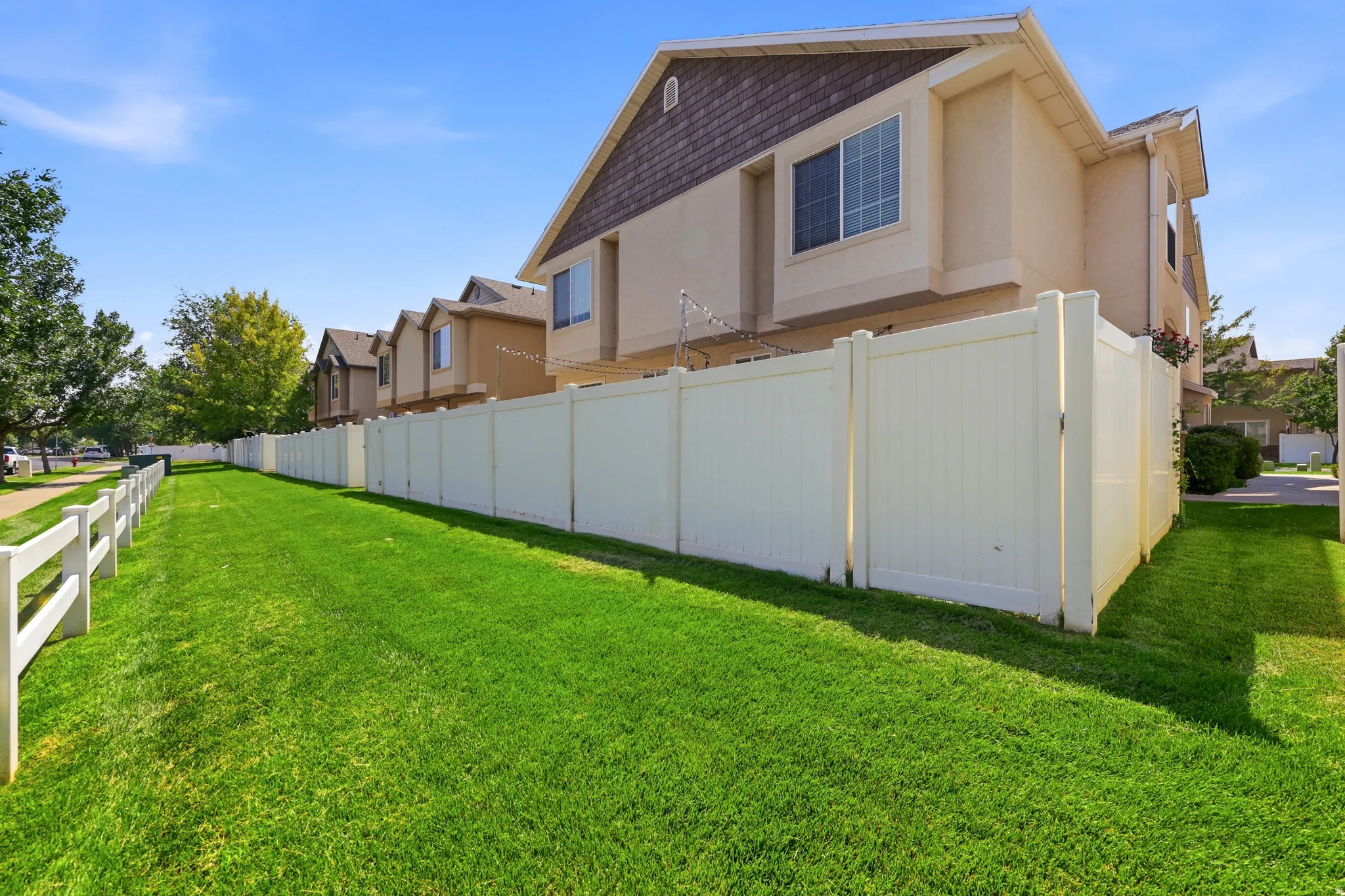 Expansive green space featuring a white vinyl privacy fence and a split-rail fence
