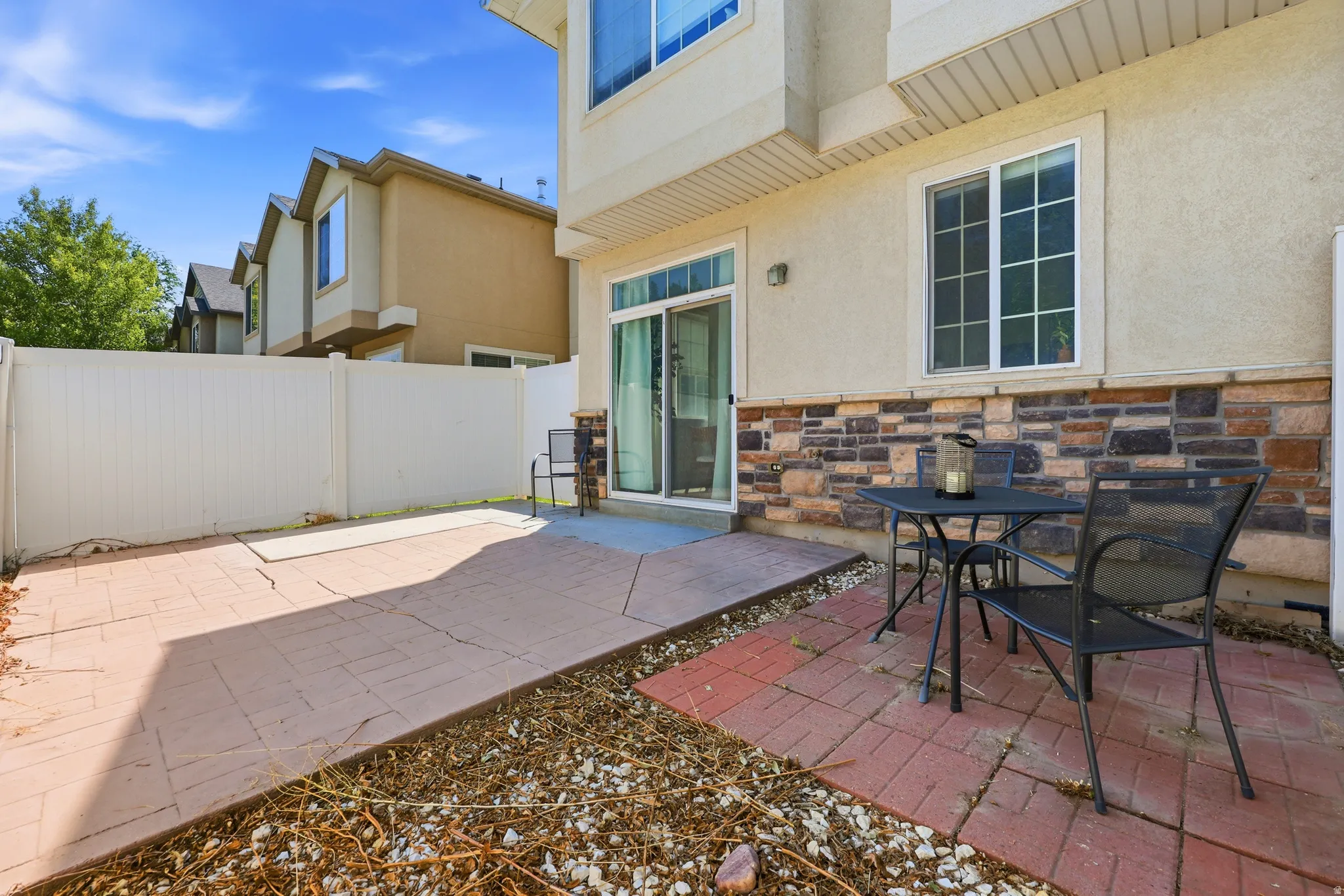 Private patio area featuring a sliding glass door, stone veneer detailing, and a white privacy fence