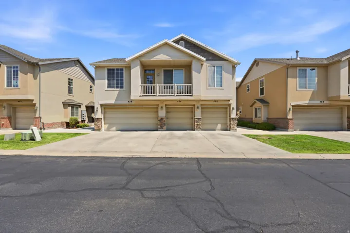 Stucco exterior with stone accents, balcony with white railing, paved driveway, and attached garages