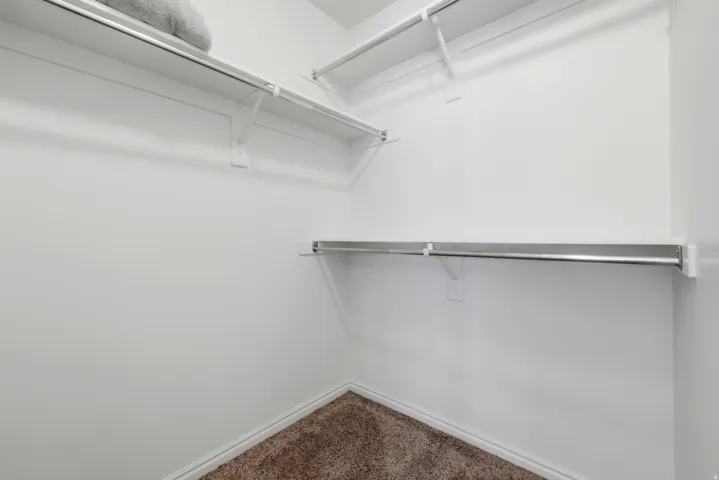 White walls with brown carpet flooring, featuring multiple white shelves with metal hanging rods