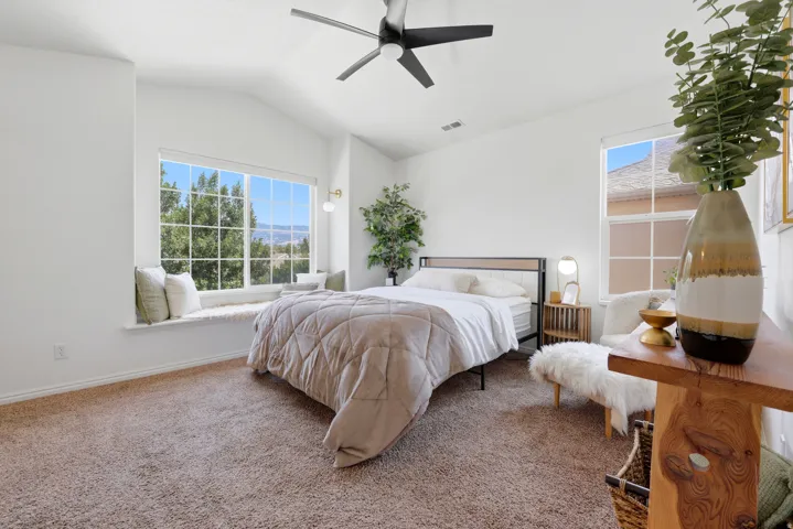 Vaulted ceiling, ceiling fan, carpet flooring, window seat, and large windows