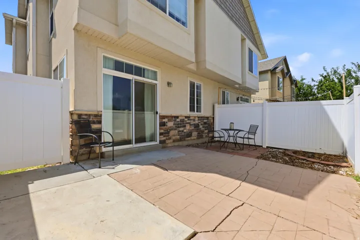 Private patio space featuring a sliding glass door, white privacy fencing, and a stone veneer foundation