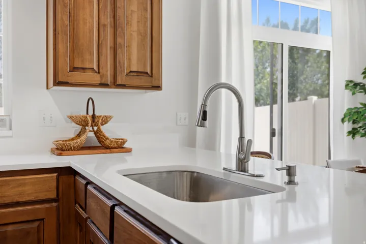 Stainless steel sink with a pull-down faucet, white solid surface countertop, and wood-finish cabinetry