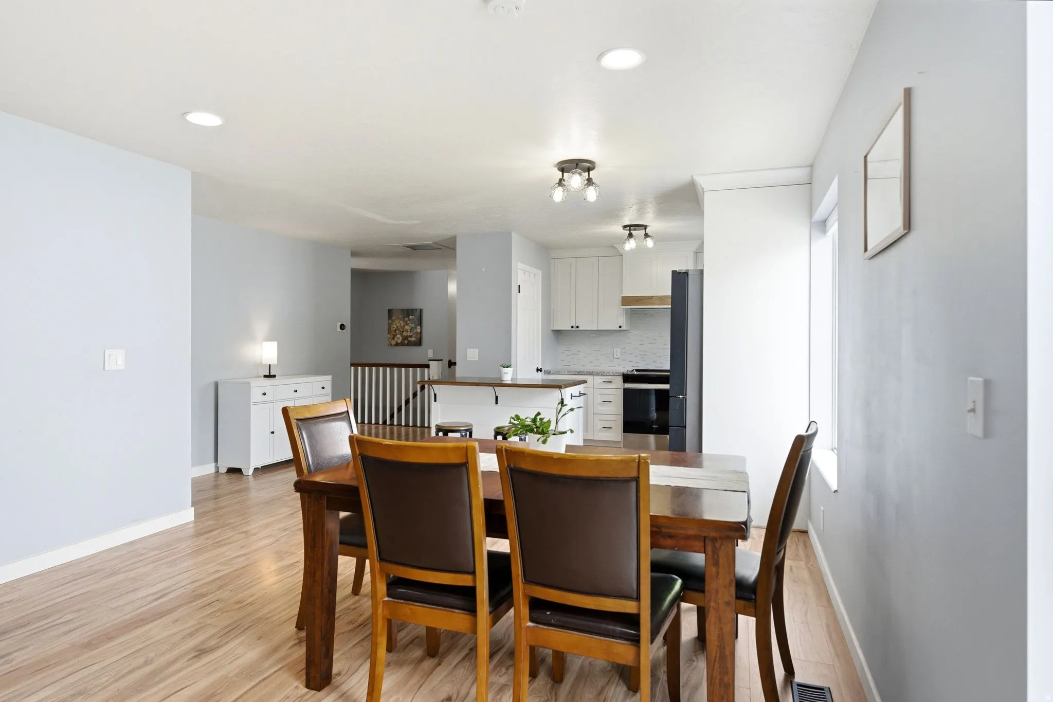 Wood-finish flooring throughout, recessed ceiling lighting, and a kitchen with white cabinetry, a tiled backsplash, and stainless steel appliances