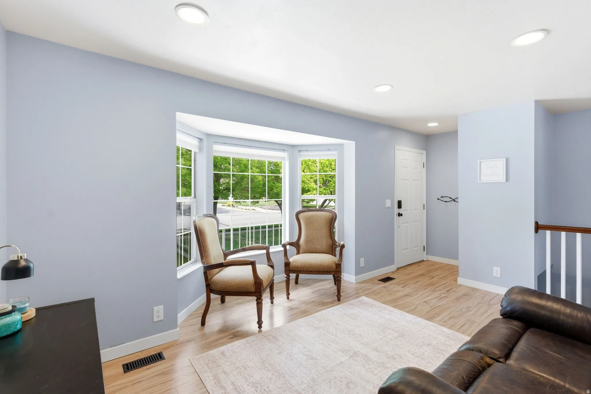 Bay window, recessed lighting, wood-finish flooring, white paneled door, and a staircase with white spindles