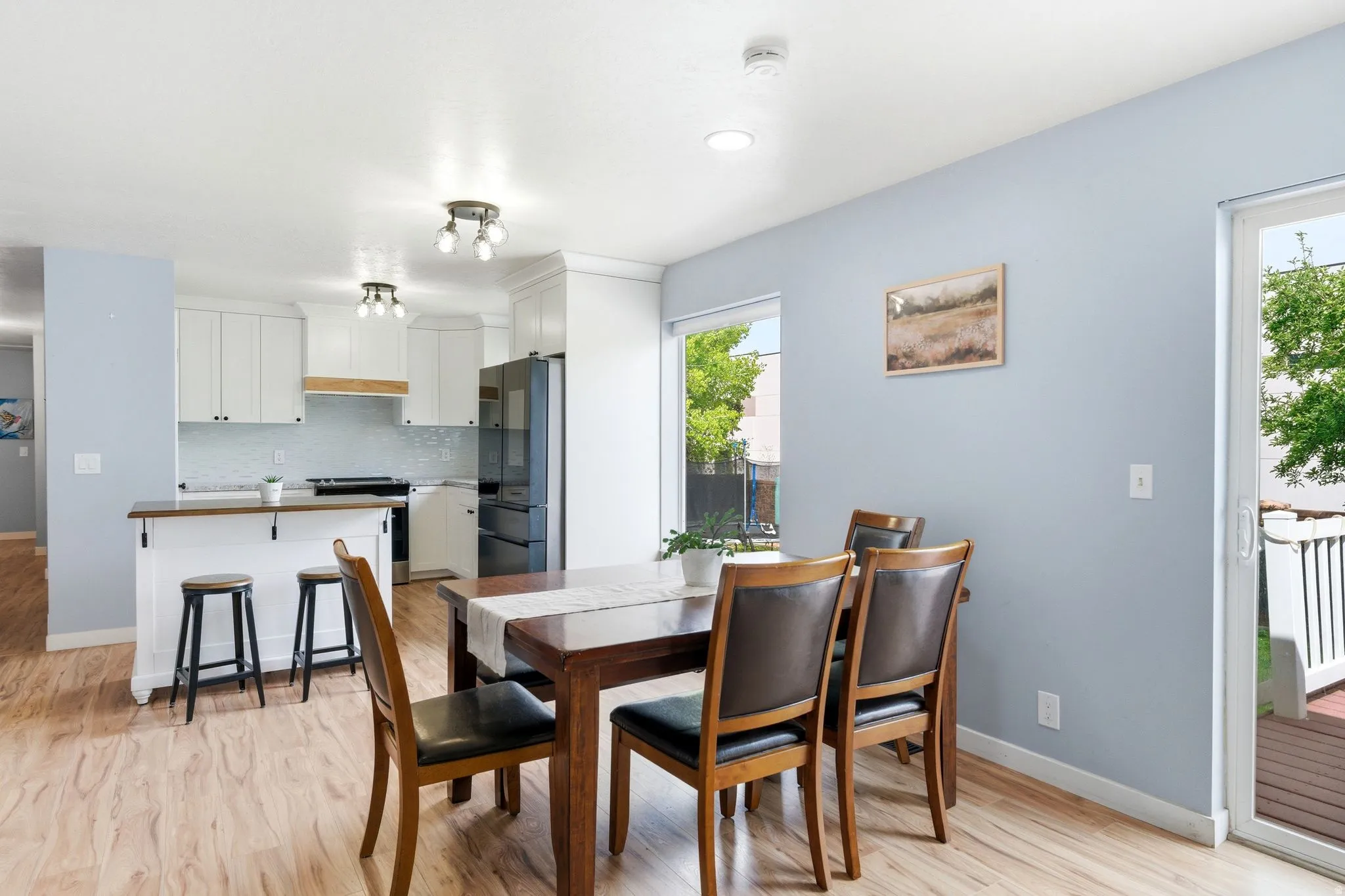 Open-concept living space with wood-finish flooring, white cabinetry, a kitchen island with seating, recessed lighting, and a sliding glass door