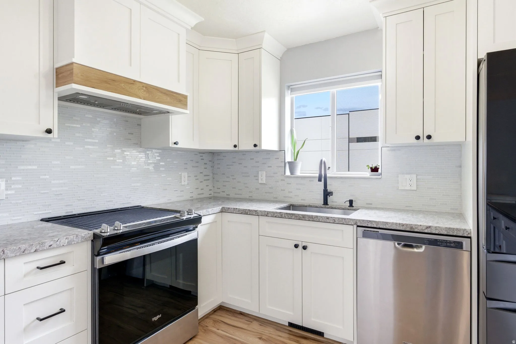 White shaker cabinetry, light-toned countertops, full tile backsplash, stainless steel appliances, and wood-finish flooring