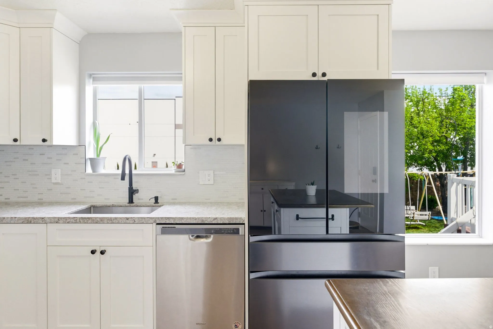 White shaker-style cabinetry with dark hardware, stainless steel sink with a dark gooseneck faucet, light-toned backsplash, granite-style countertop, and stainless steel dishwasher
