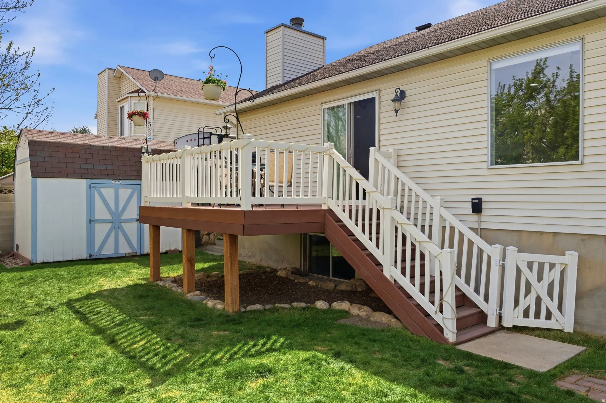 Elevated wood deck with white railings and staircase, sliding glass door access, and an adjacent utility shed