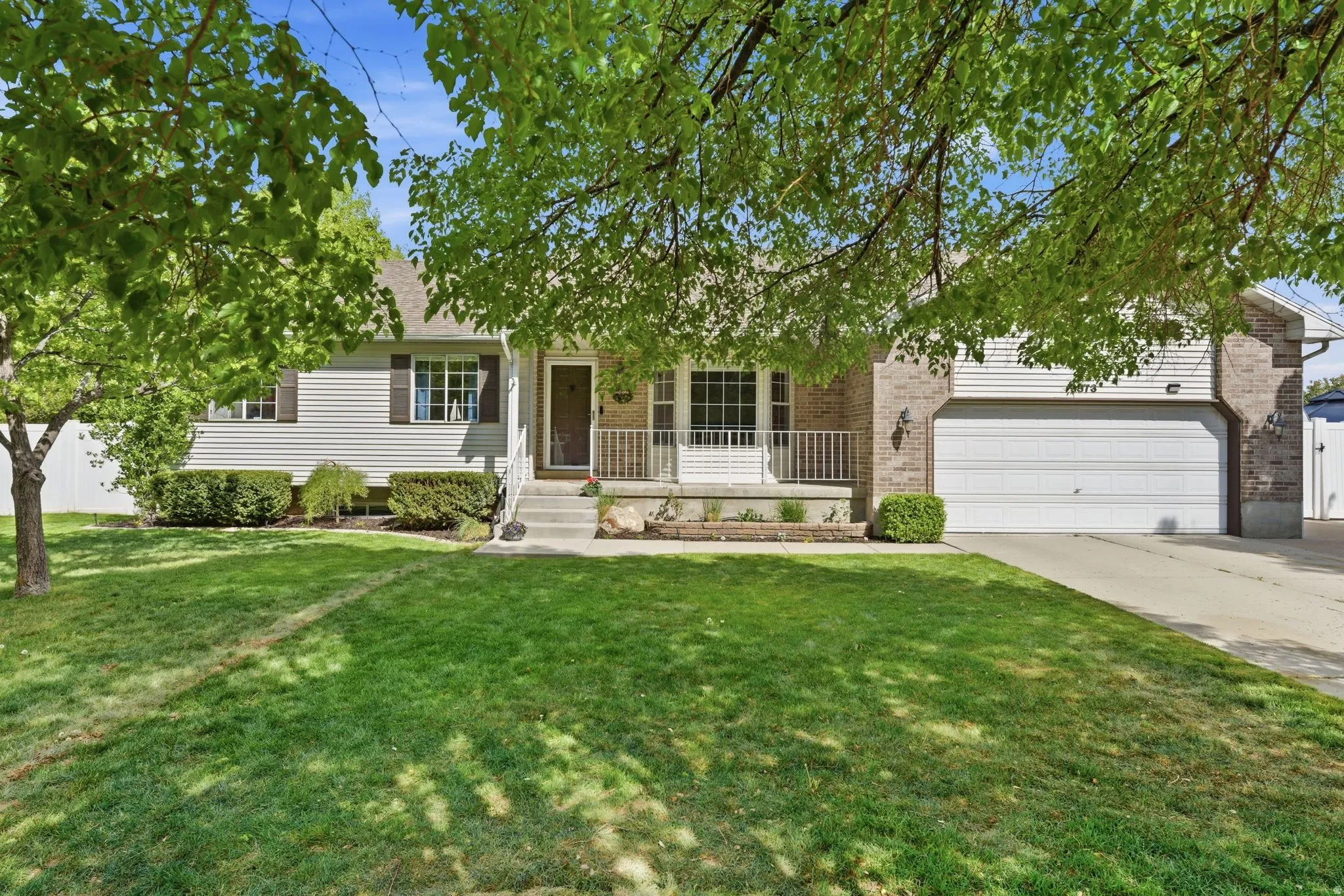 Exterior with brick and siding facade, covered entry porch, front yard with mature trees, and an attached garage
