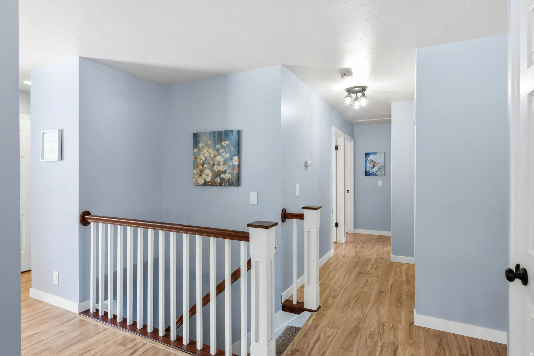 Wood-finish flooring throughout, white baluster railing with wood handrail, and overhead lighting fixtures