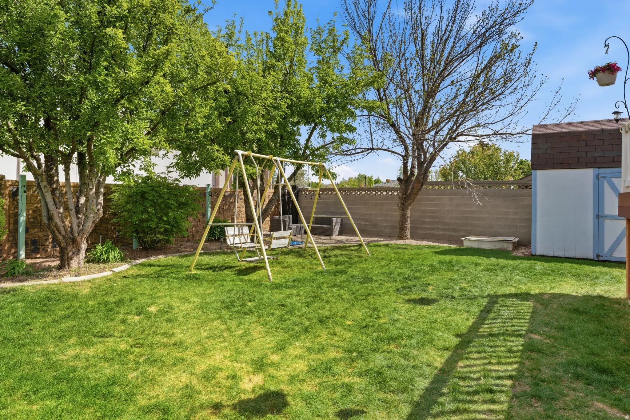 Expansive green lawn, mature trees, concrete block perimeter fencing, and a storage shed with shingle roofing