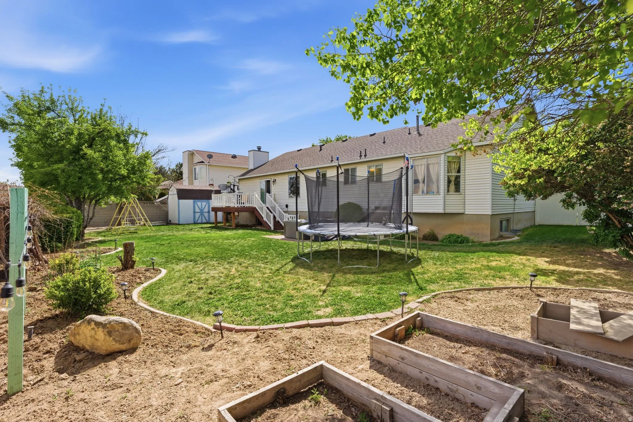 Expansive backyard featuring a manicured lawn, a raised wooden deck, a storage shed, and raised garden beds