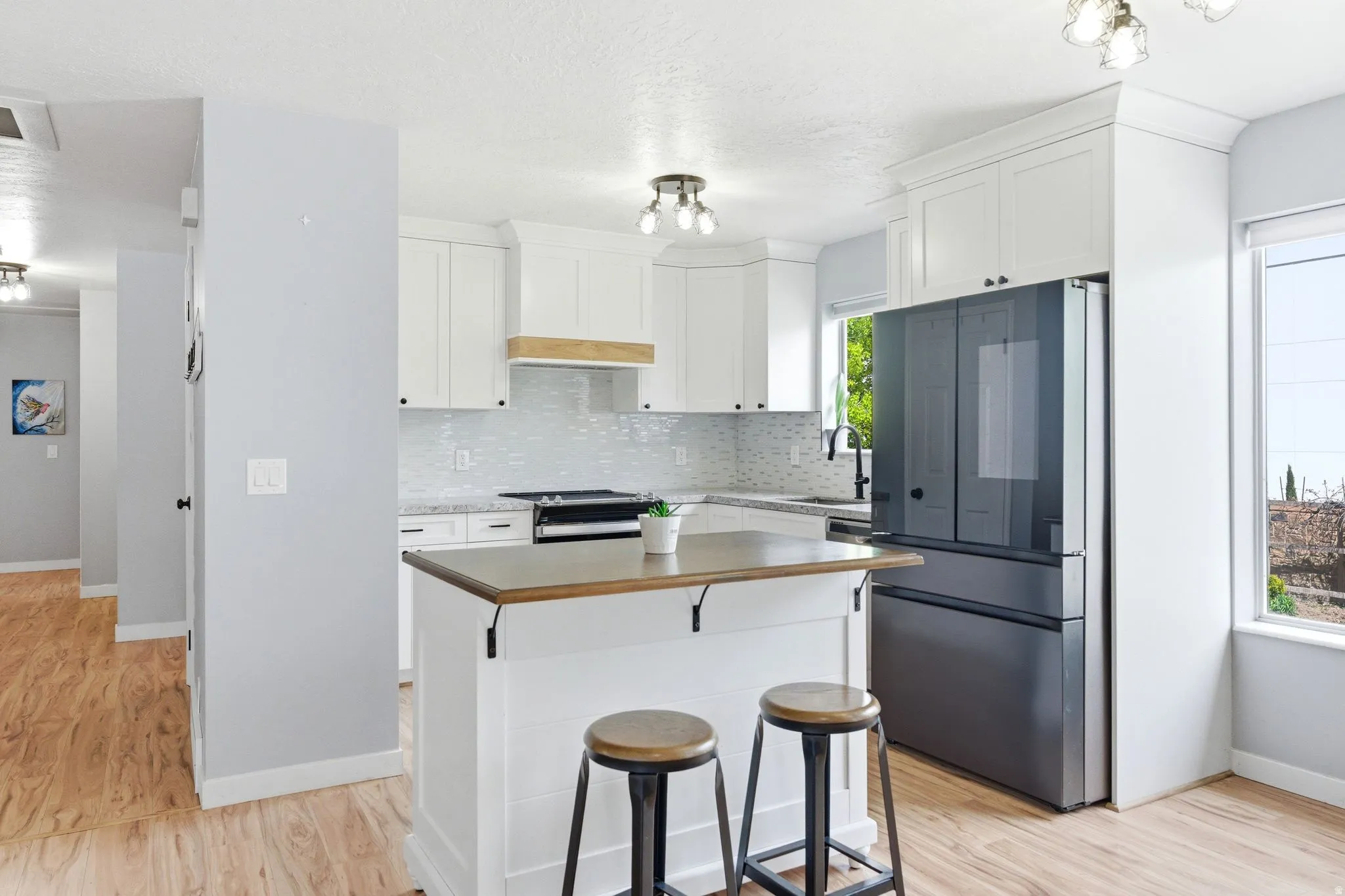 Kitchen featuring white shaker cabinetry, wood-finish flooring, a kitchen island with a wood-finish countertop, and a tiled backsplash