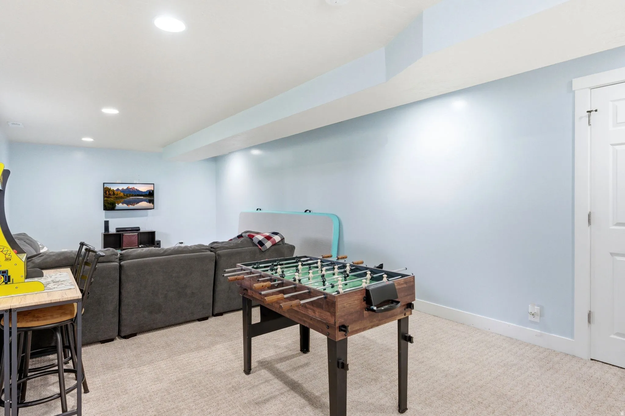 Recessed lighting, wood-finish flooring, light blue wall paint, white trim, and a white interior door