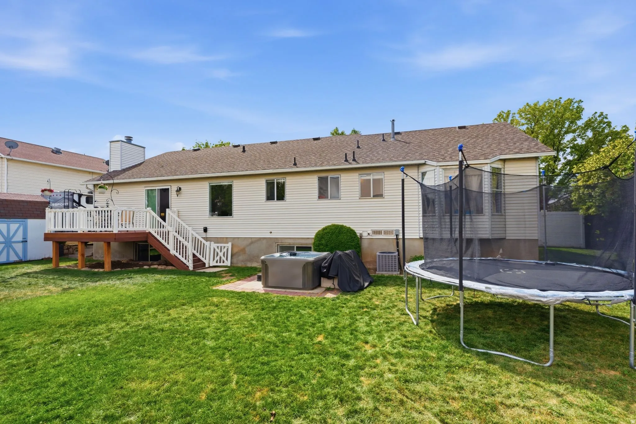 Expansive backyard with a raised wooden deck featuring white railings, a sliding glass door, and a built-in hot tub