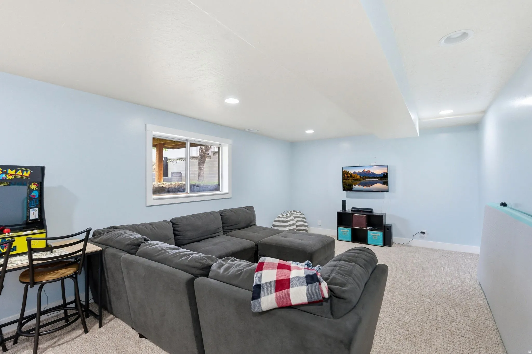 Recessed lighting, light blue wall paint, window with white trim, and light-toned carpet flooring