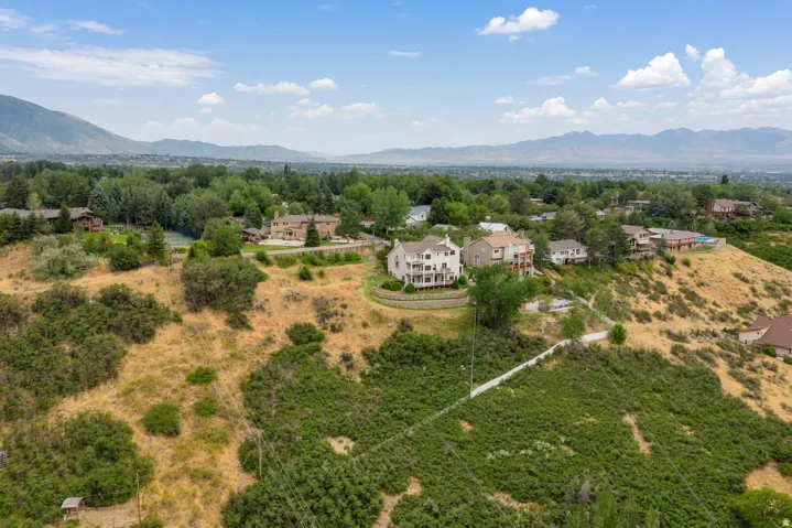 Hillside property featuring a multi-story residence with balconies, a stone retaining wall, and mature landscaping