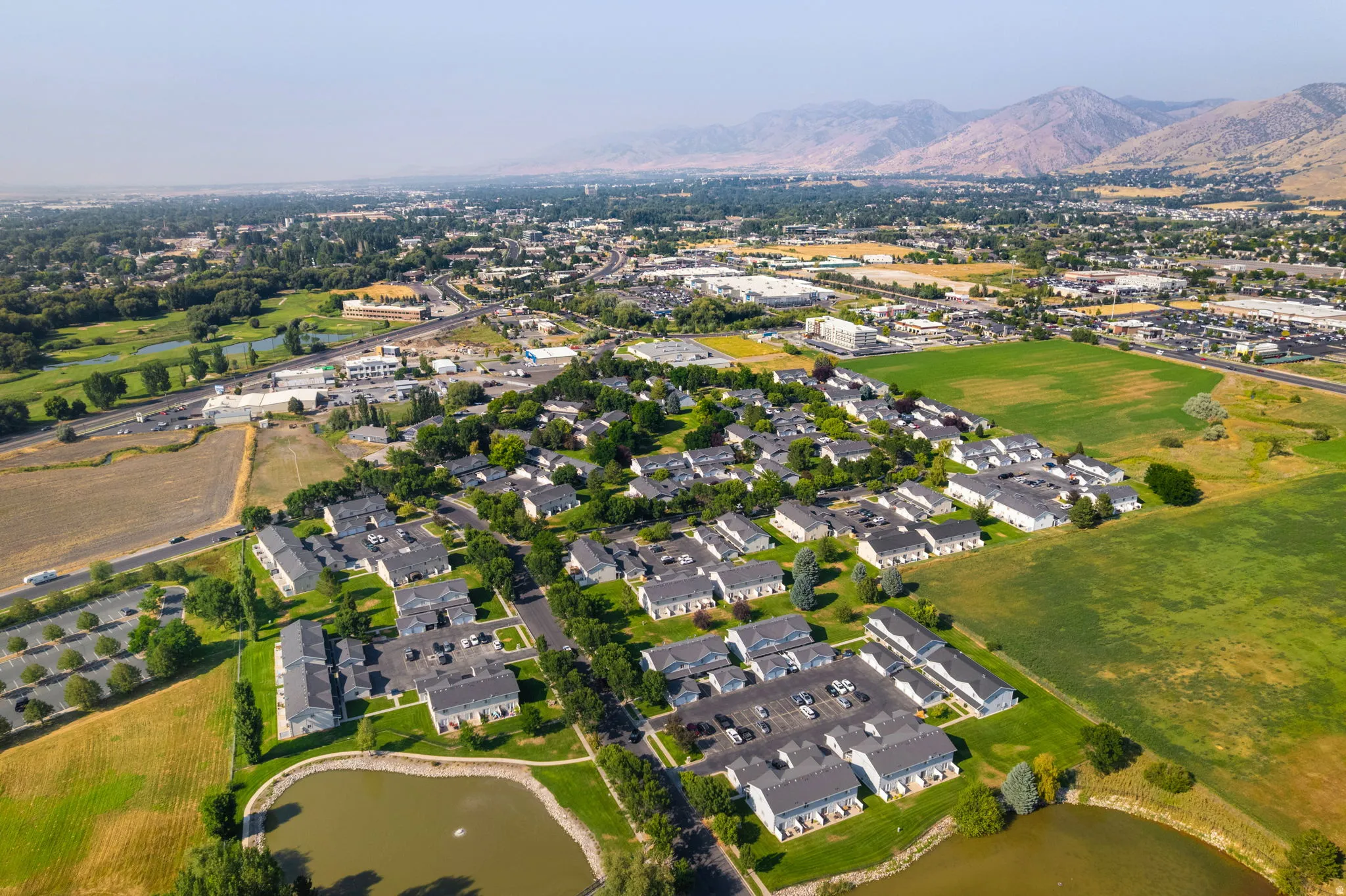 Community with residential buildings, green spaces, and a pond