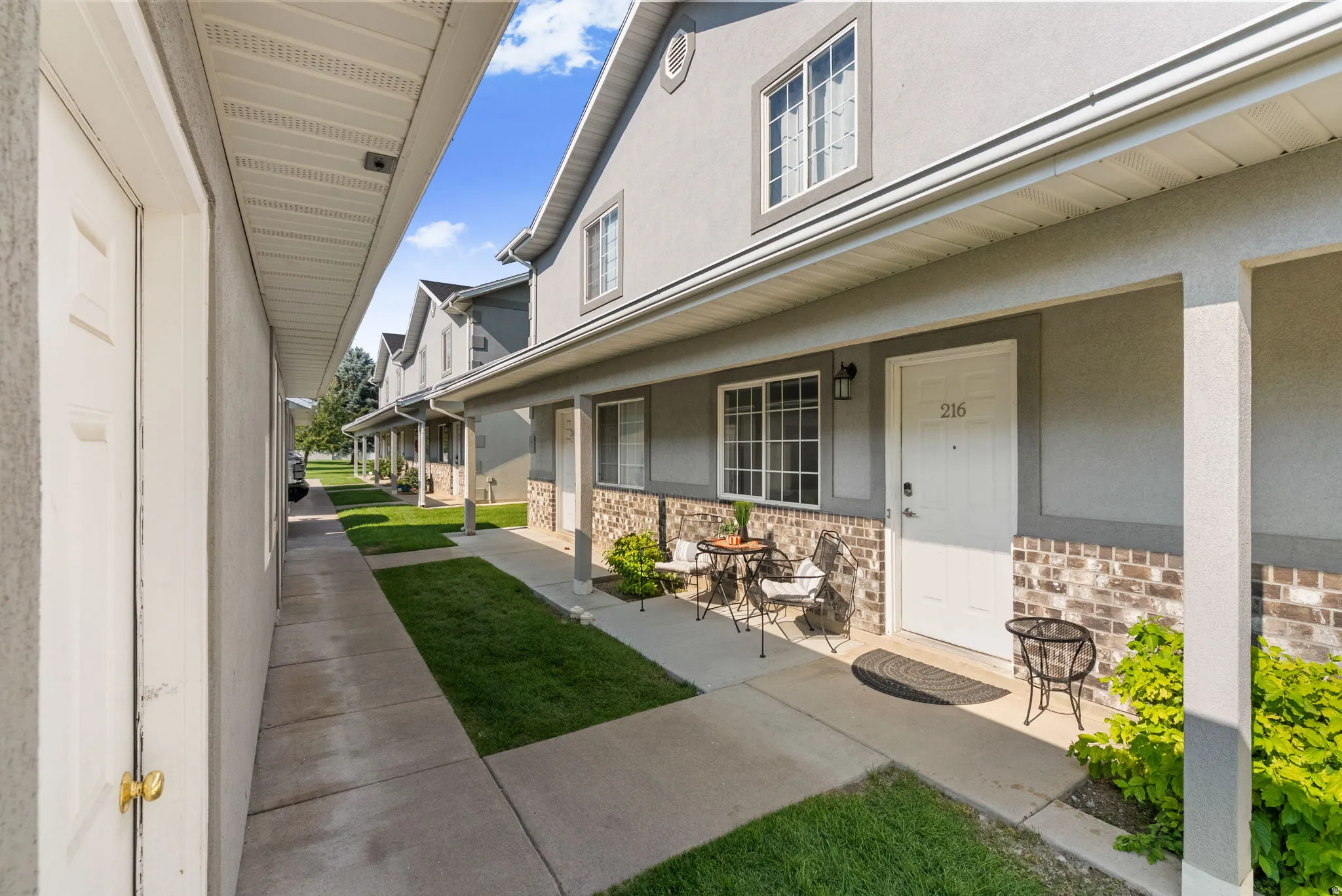 Exterior featuring a stucco facade, brick wainscoting, covered porch, multiple windows, and a paved walkway