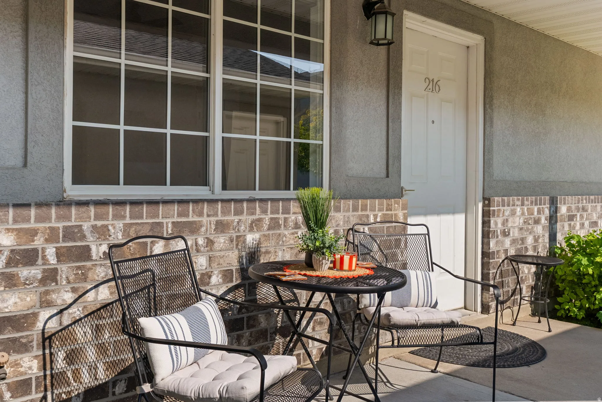 Porch entrance featuring a white panel door, decorative outdoor light fixture, windows with grid patterns, and a brick facade
