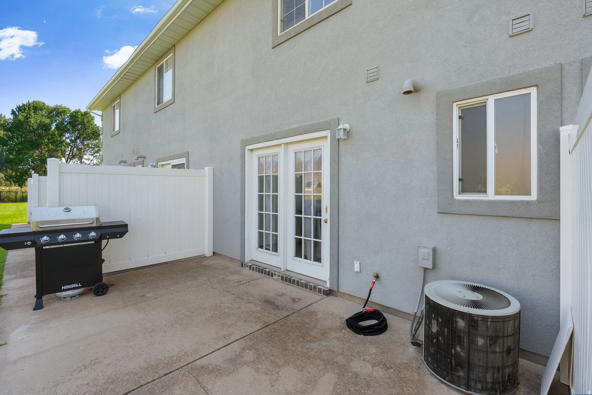 Rear concrete patio with white privacy fencing, double glass-paned doors, and exterior lighting