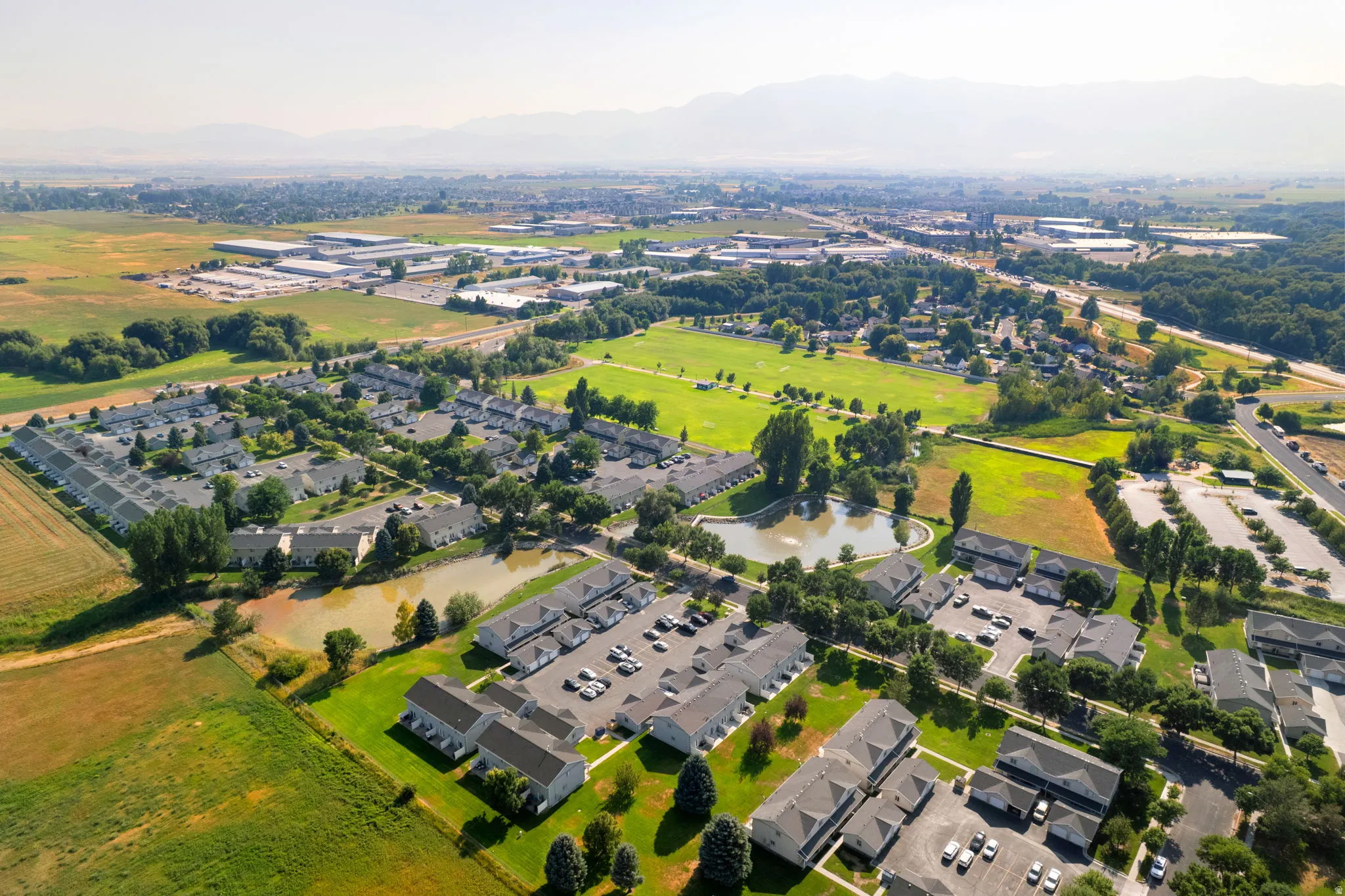 Expansive residential area with multiple multi-unit buildings, surrounded by green fields, and featuring two ponds