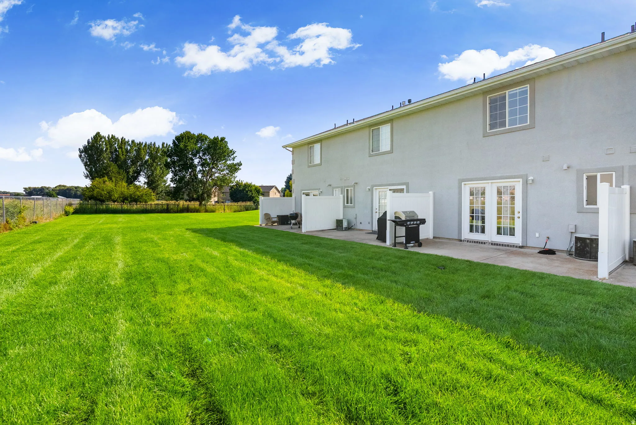 Expansive rear yard featuring a large grass area, a concrete patio, and white privacy fencing