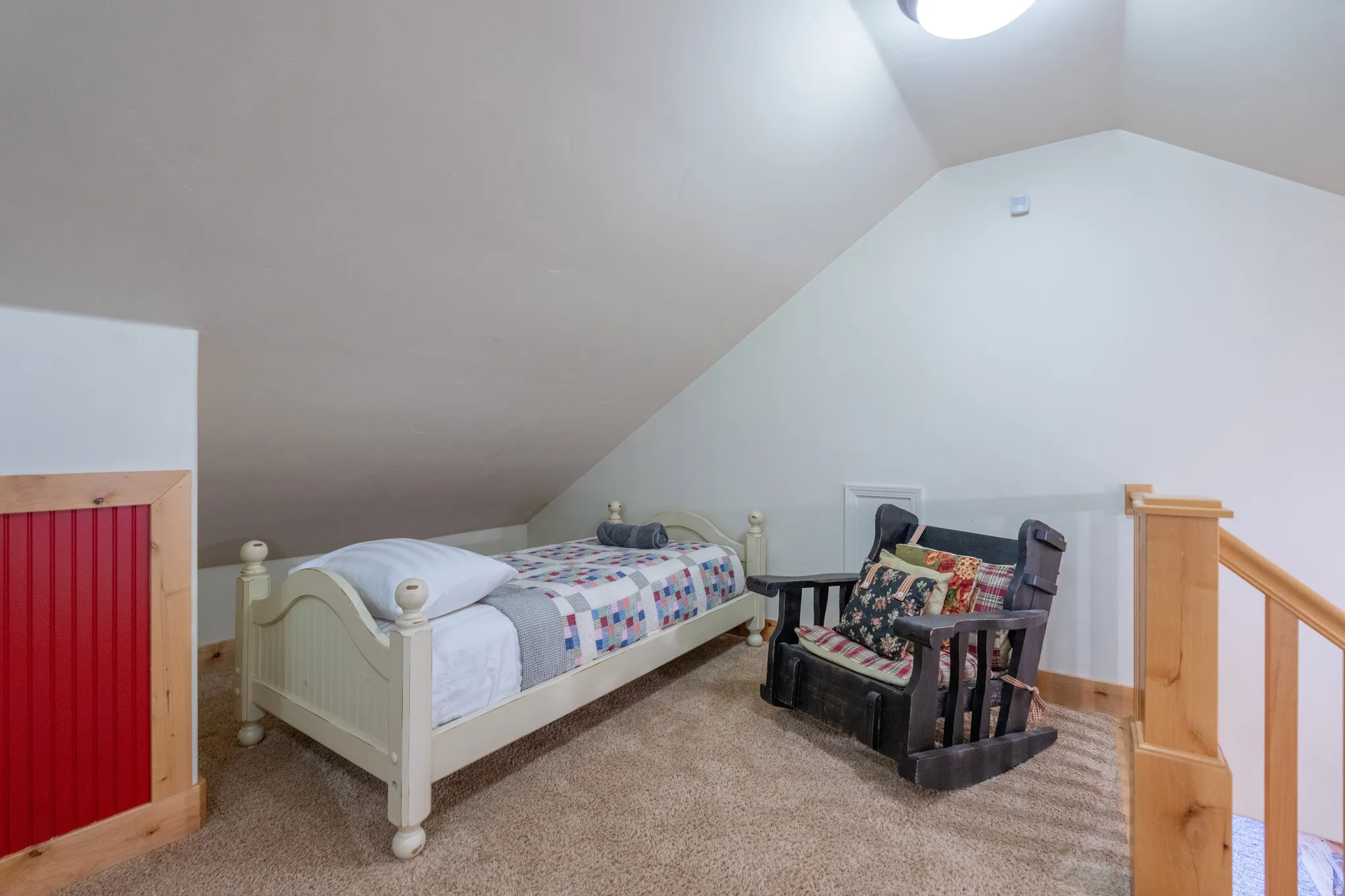 Carpeted upper-level space featuring a sloped ceiling, wood-finish railing, and red beadboard paneling with natural wood trim
