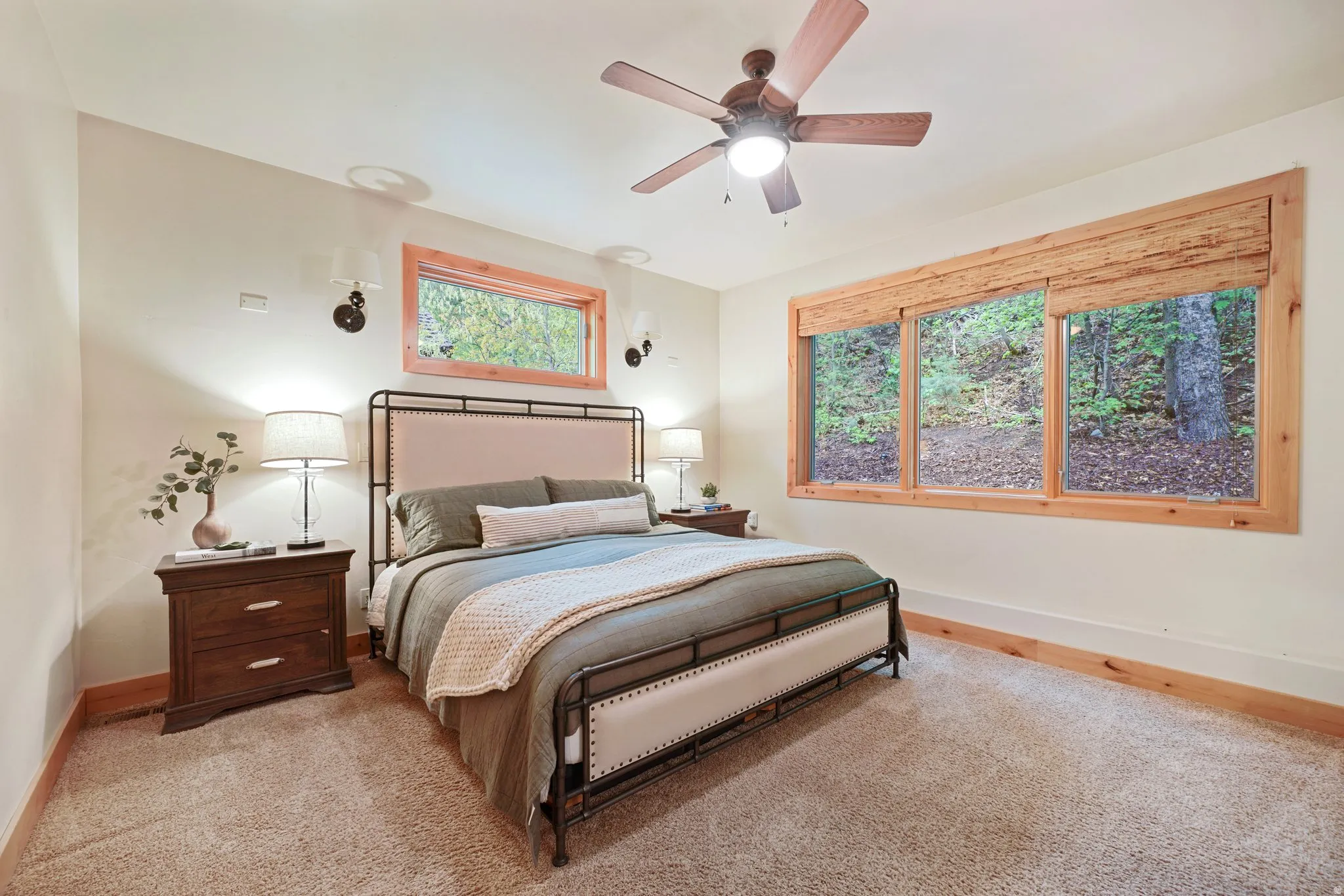 Carpeted flooring, natural wood window frames, sconce lighting, and a ceiling fan with integrated lighting