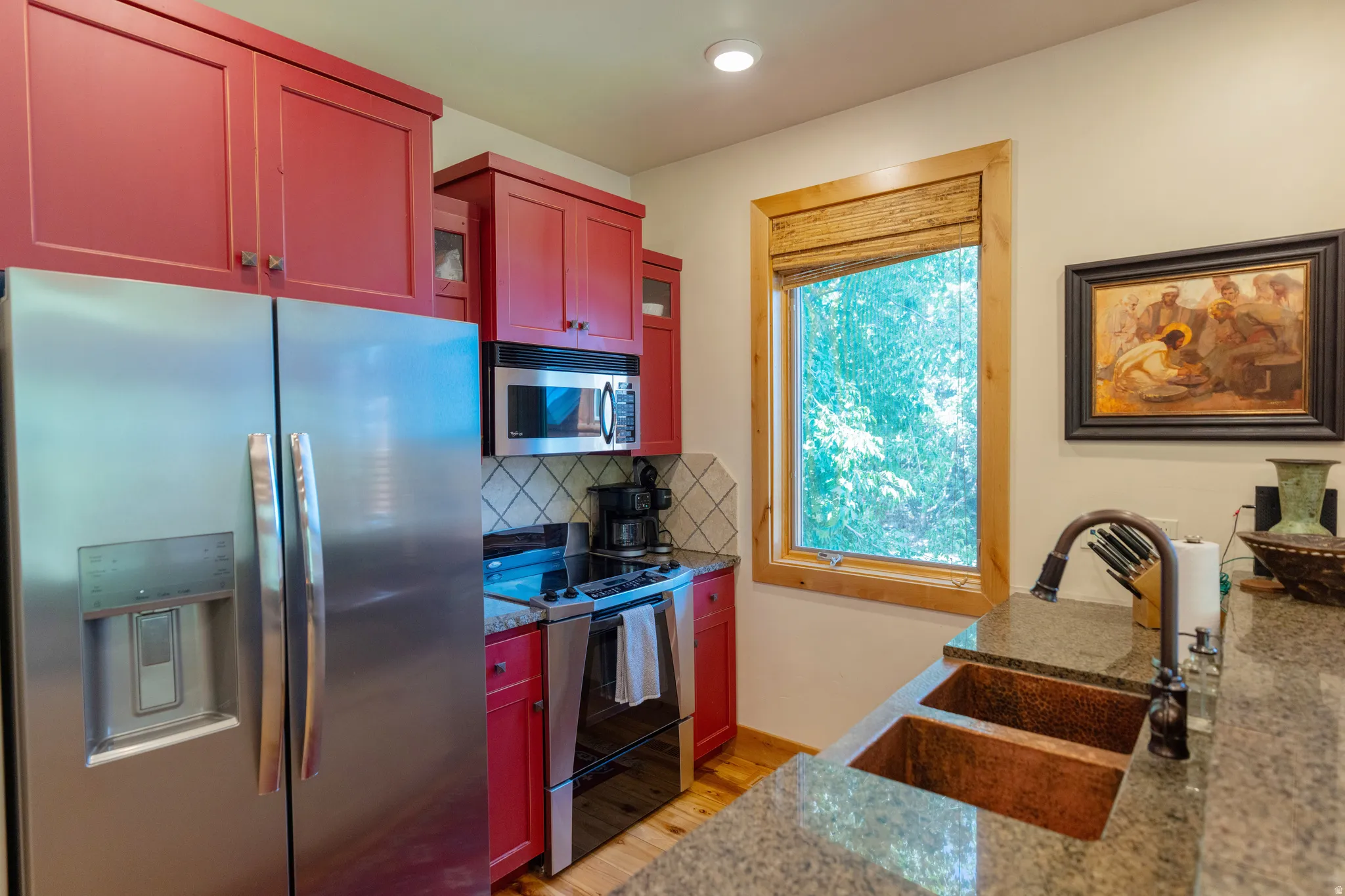Kitchen featuring red cabinetry, stainless steel appliances, granite countertops, and a copper double-basin sink with a gooseneck faucet