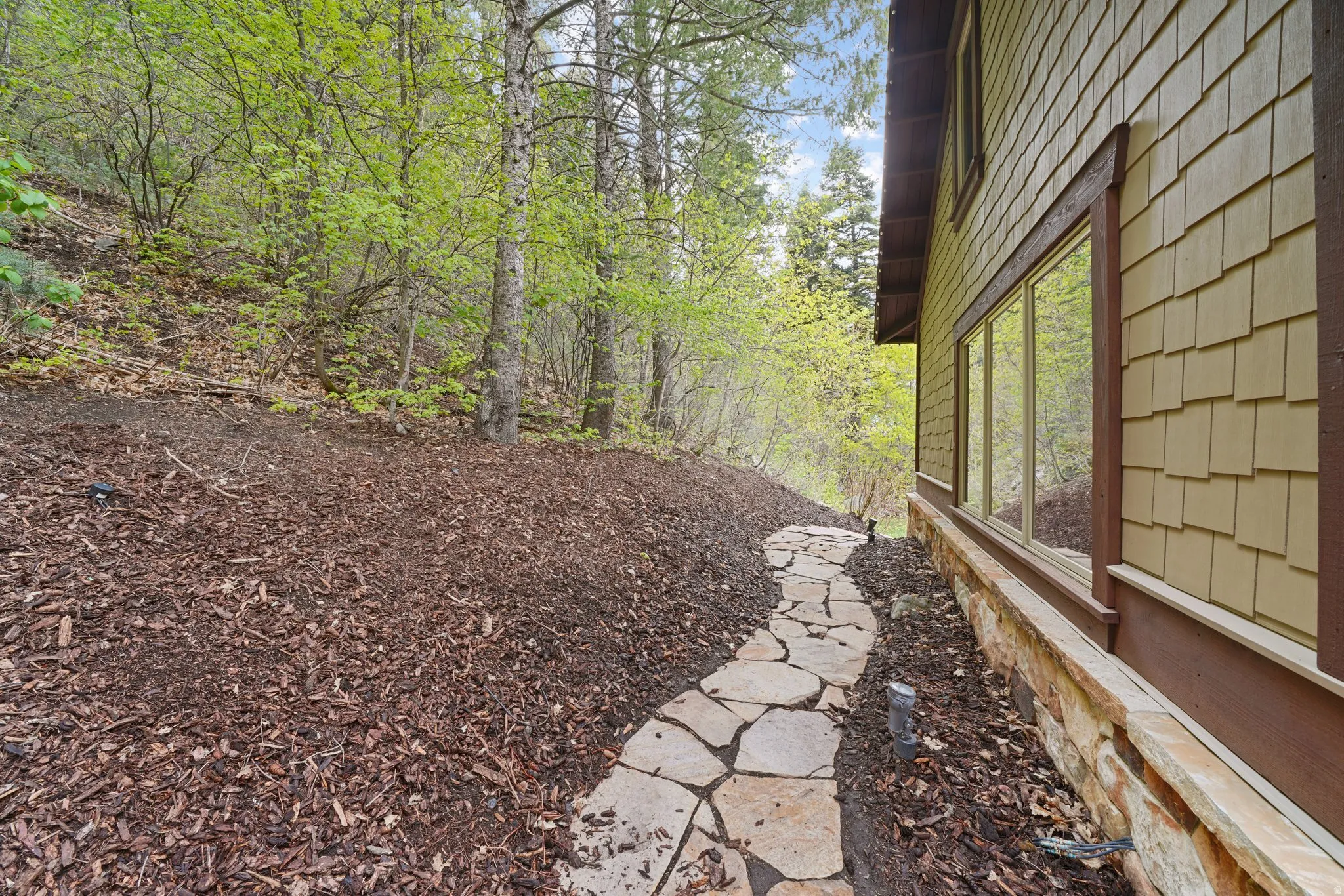 Stone pathway leading to a residence with wood shake siding, a stone foundation, and a series of large windows