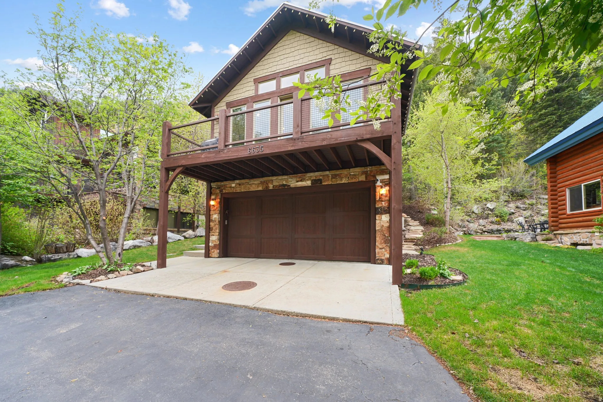 Stone-clad garage entry with a two-car capacity, covered by an upper-level balcony featuring wood railing
