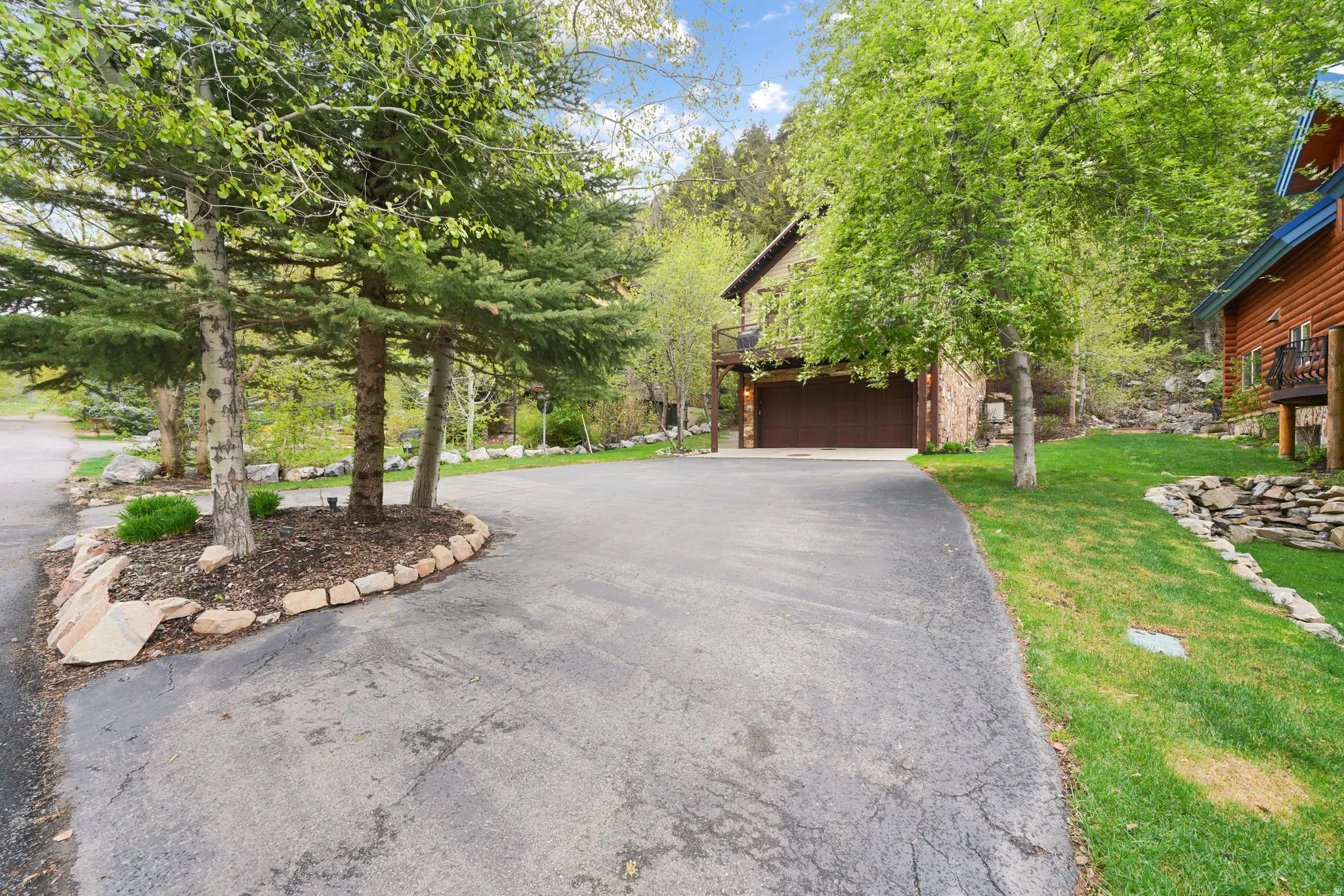 Paved driveway with a stone-edged planting bed, mature trees, and a two-car garage