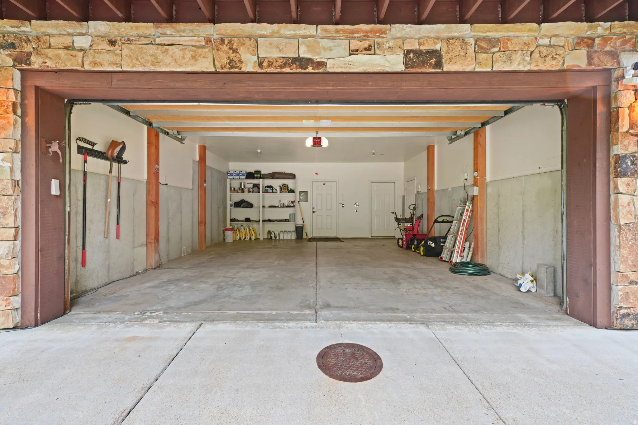 Spacious attached garage with concrete flooring, exposed wood beams, and a stone facade