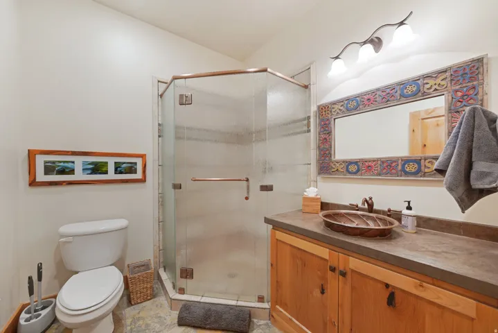 Corner glass shower enclosure with bronze-finish trim, wood vanity with a vessel sink, and a decorative framed mirror