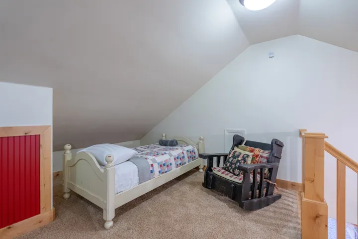 Carpeted upper-level space featuring a sloped ceiling, wood-finish railing, and red beadboard paneling with natural wood trim