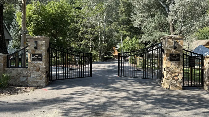 Stone pillar entrance with wrought iron gates, surrounded by mature trees