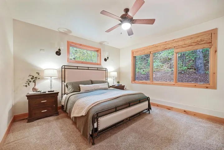 Carpeted flooring, natural wood window frames, sconce lighting, and a ceiling fan with integrated lighting