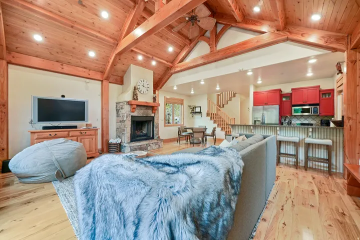 Vaulted wood-finish ceilings with exposed beams, stone-clad fireplace, wood-finish flooring, and a kitchen with red cabinetry