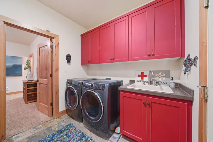 Built-in cabinetry with red finishes, a utility sink with a chrome faucet, and dark stone-finish countertops