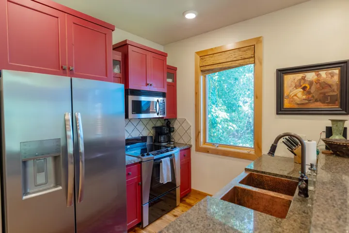 Kitchen featuring red cabinetry, stainless steel appliances, granite countertops, and a copper double-basin sink with a gooseneck faucet