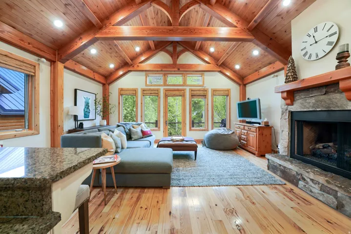Vaulted wood-paneled ceiling with exposed wood beams, stone-clad fireplace with wood mantel, wood-finish flooring, and a granite-finish countertop
