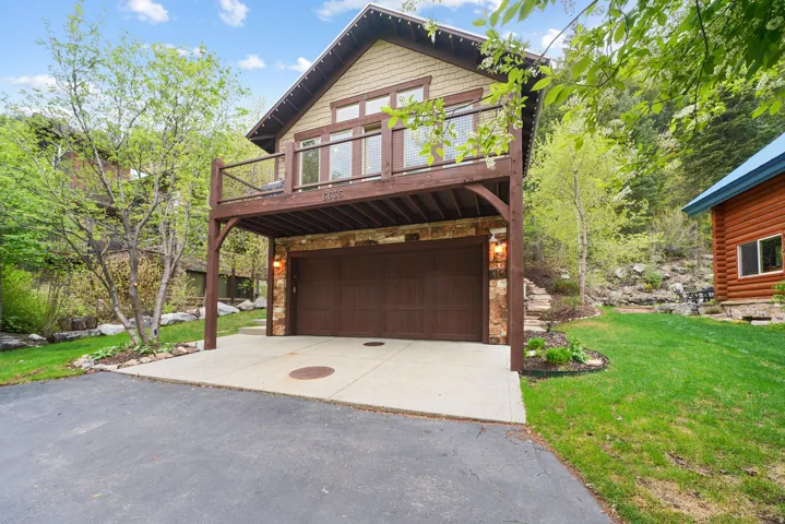 Stone-clad garage entry with a two-car capacity, covered by an upper-level balcony featuring wood railing