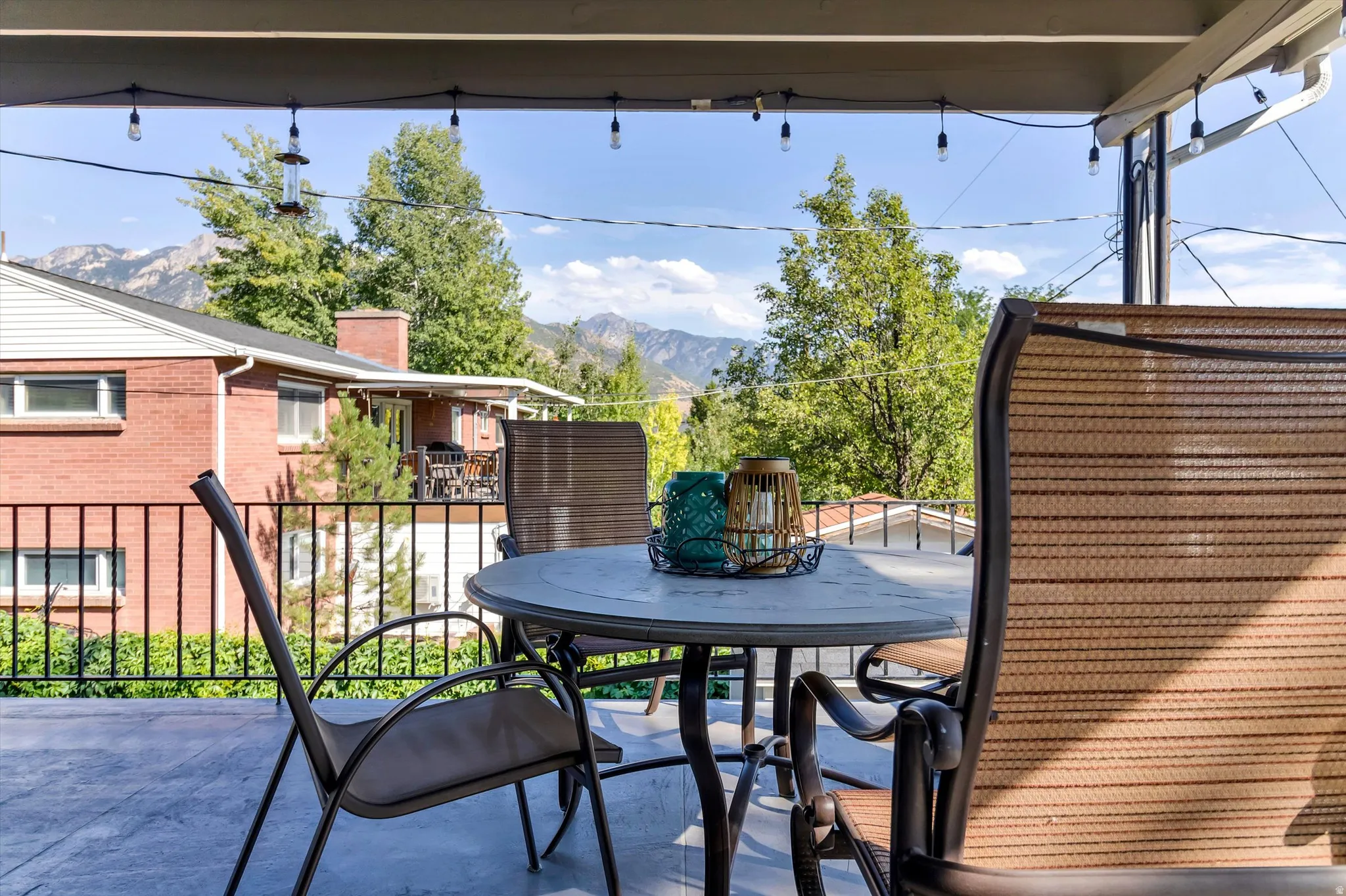 Covered patio space featuring an overhead string lighting system, mountain backdrop, and black metal railing