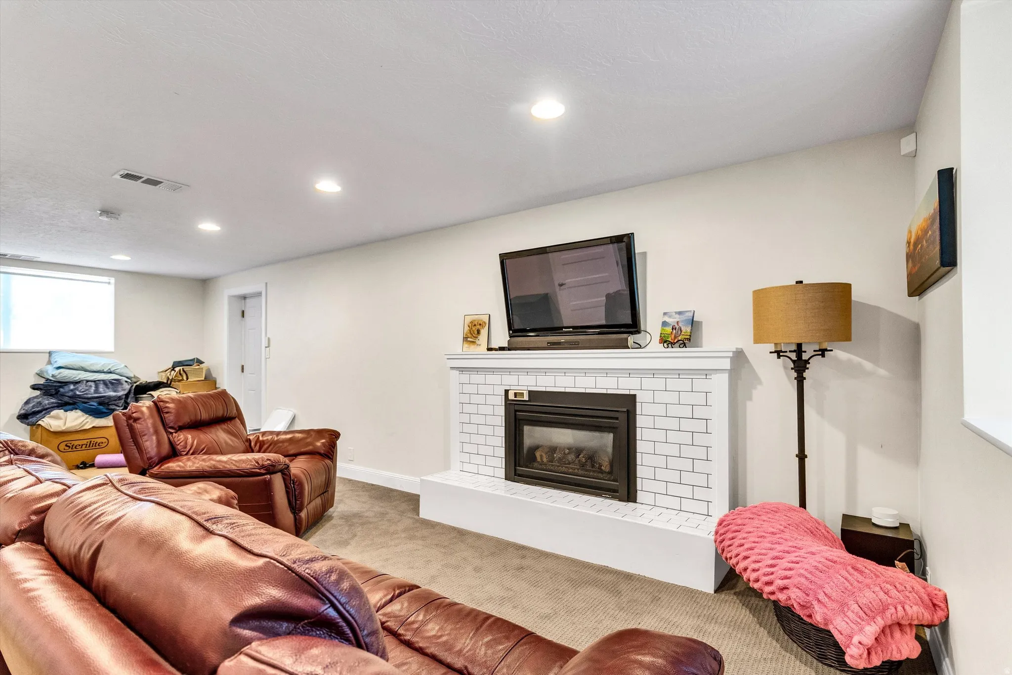 Recessed lighting illuminating a spacious room featuring a fireplace with white subway tile surround and mantel