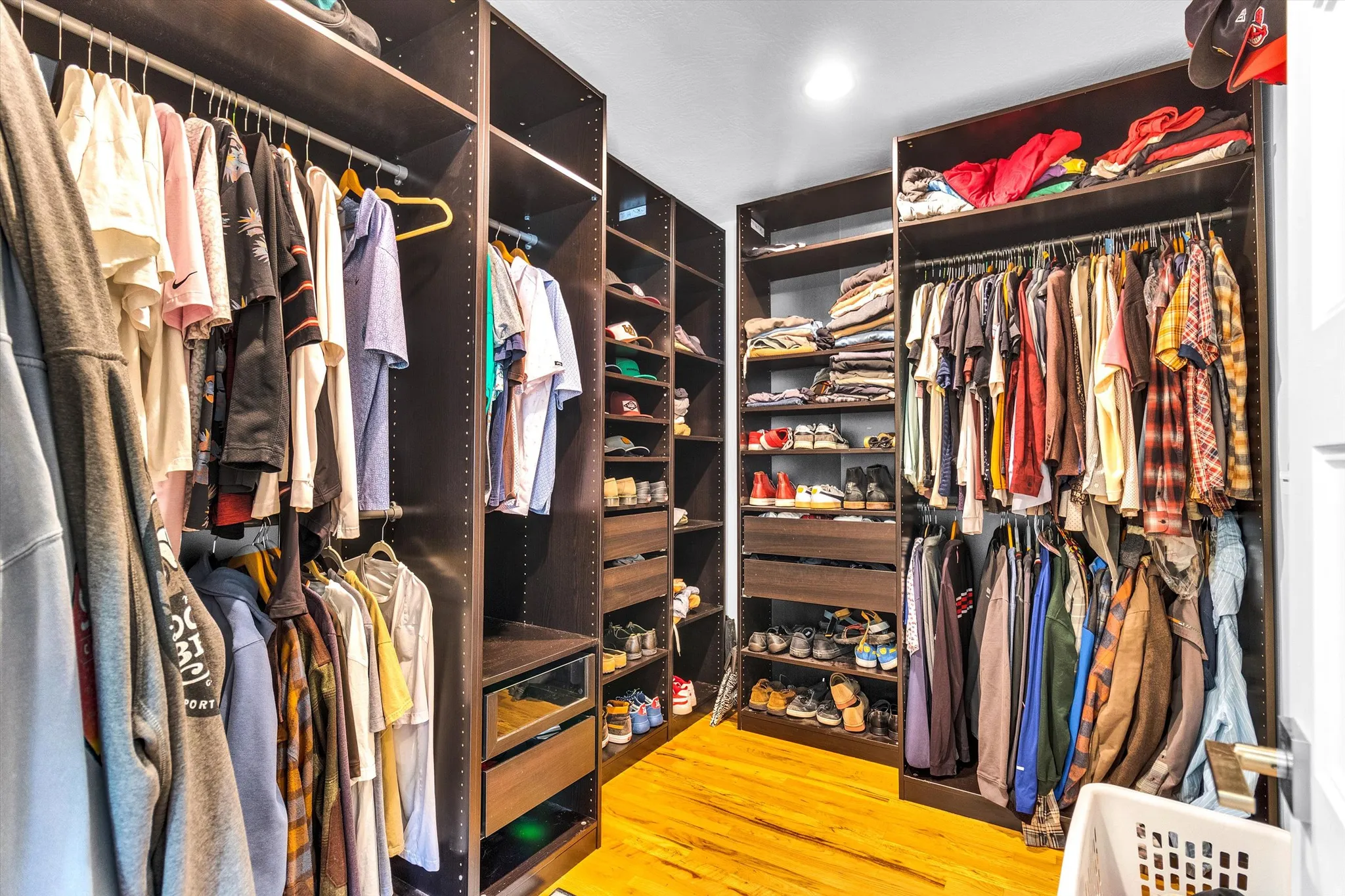 Walk-in closet featuring custom dark wood-finish cabinetry, ample hanging space, built-in shelving, organized shoe storage, and wood-finish flooring