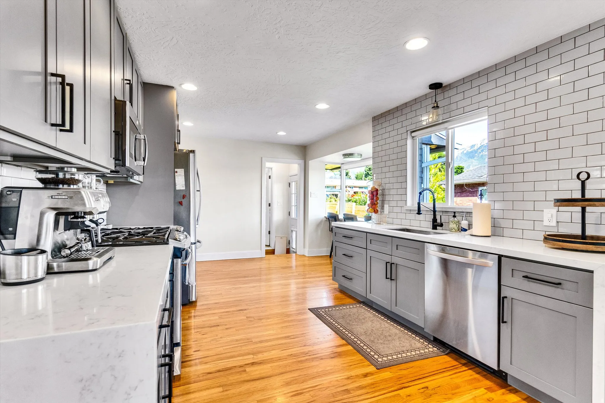 Contemporary kitchen featuring light wood-finish flooring, recessed lighting, white perimeter countertops, and a subway tile backsplash